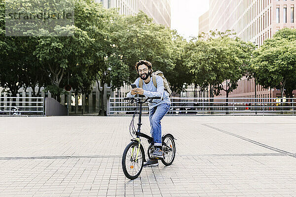 Lächelnder Mann  der auf dem Fahrrad sitzt und sein Telefon benutzt