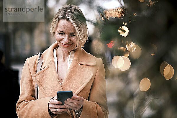 Lächelnde Frau  die ihr Mobiltelefon benutzt