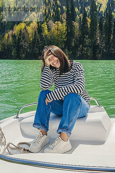 Glückliche junge Frau sitzt mit dem Kopf in den Händen auf einem Boot am Ritsa-See