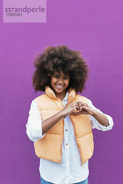 Girl gesturing heart shape against purple background
