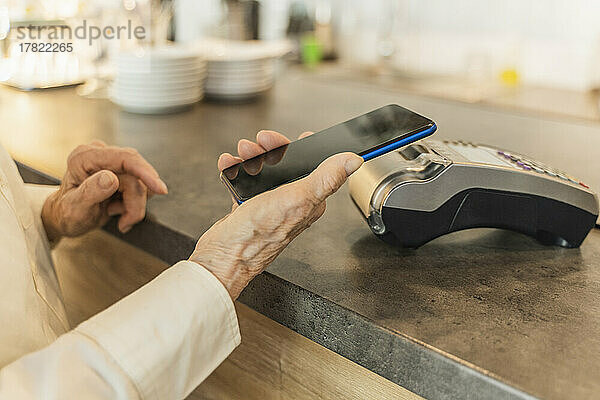 Ältere Frau bezahlt per Mobiltelefon im Café
