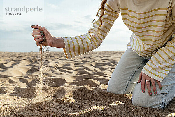 Sand tropft aus der Hand einer Frau am Strand