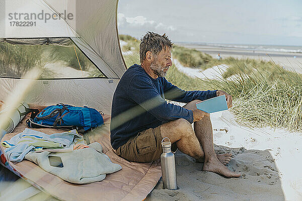 Reifer Mann liest an einem sonnigen Tag am Strand ein Buch