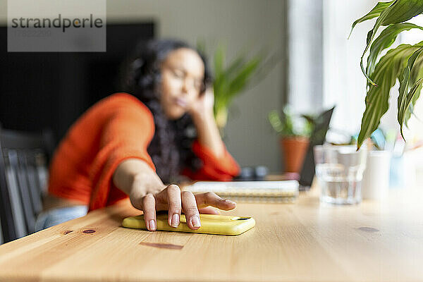Freiberufler berührt Smartphone auf Schreibtisch im Heimbüro