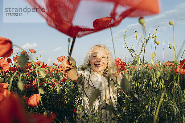 Glückliches Mädchen  das mit Schmetterlingsnetz im Mohnfeld spielt