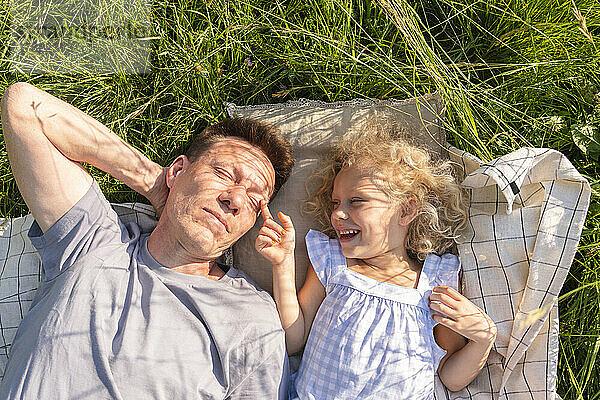 Happy girl lying with father on picnic blanket amidst grass