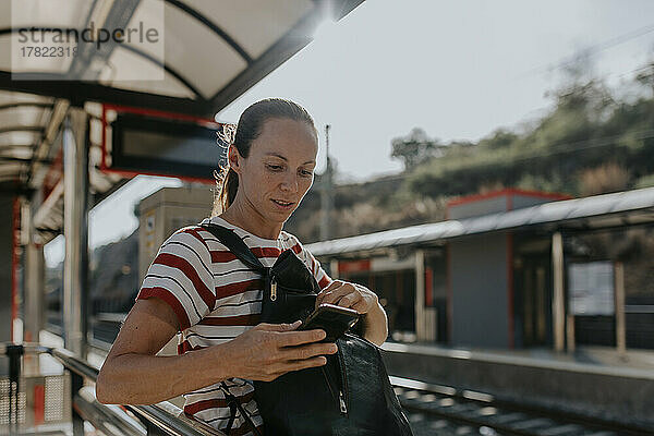 Frau benutzt Telefon und wartet am Bahnhof