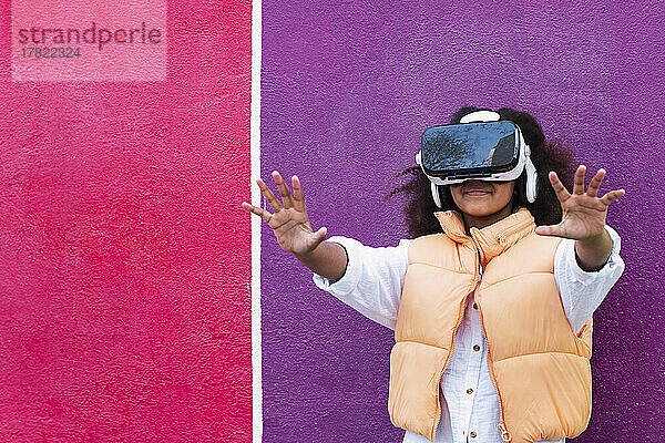 Mädchen mit Virtual-Reality-Simulator gestikuliert vor einer lila-rosa Wand