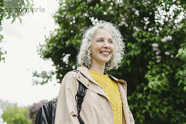 Lächelnde Frau mit Rucksack steht im Park