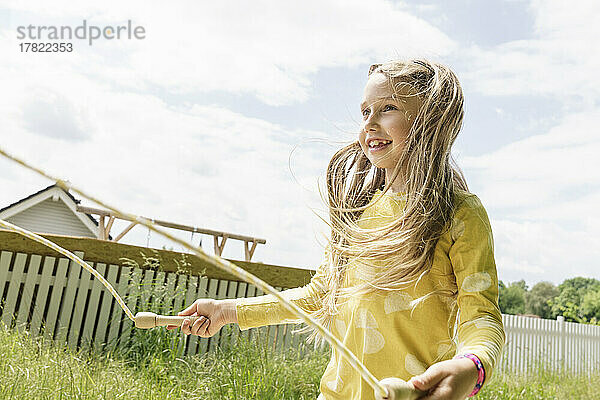 Lächelndes Mädchen  das an einem sonnigen Tag im Hinterhof mit Springseil spielt