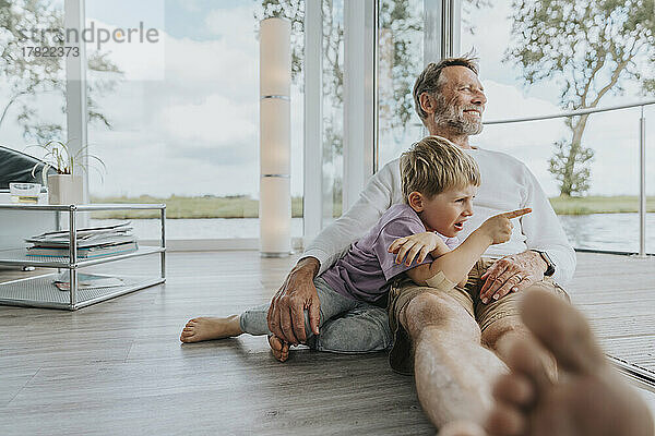 Glücklicher Vater mit Sohn  der zu Hause auf dem Boden sitzt und mit dem Finger zeigt