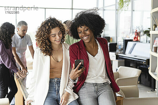 Glückliche Geschäftsfrauen  die im Büro ihr Smartphone teilen
