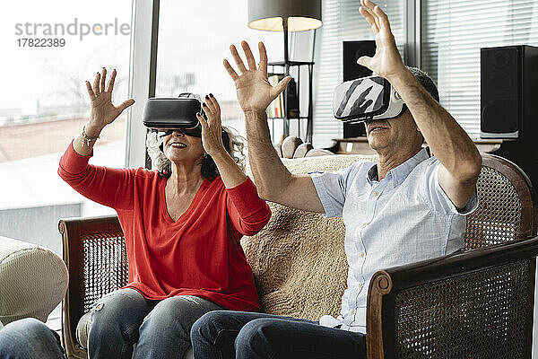 Zufriedene Geschäftskollegen mit Virtual-Reality-Simulator sitzen auf dem Sofa und gestikulieren im Büro
