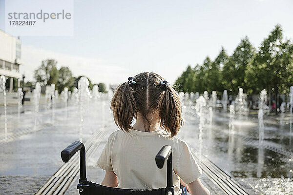 Mädchen mit Zöpfen sitzt im Rollstuhl im Park