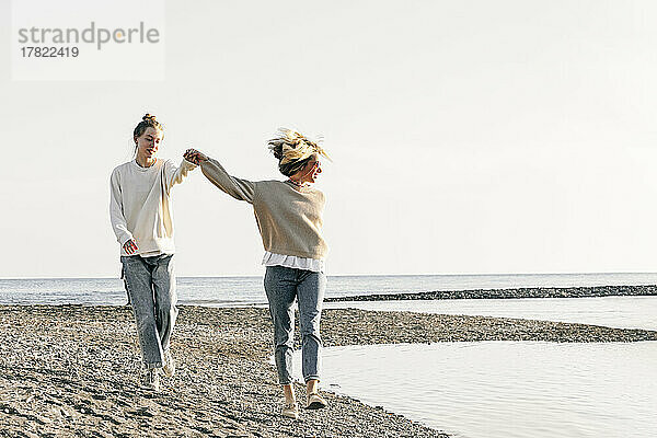 Mutter und Tochter gehen Händchen haltend gemeinsam am Strand spazieren