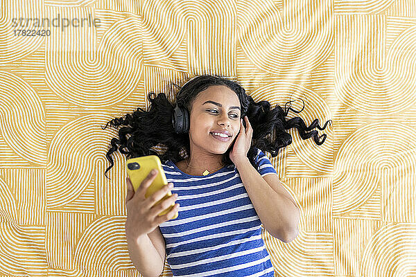 Junge Frau mit Smartphone hört Musik im Schlafzimmer