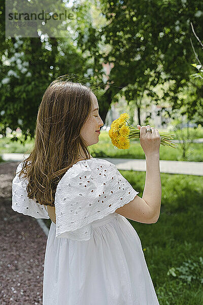 Lächelnde schwangere Frau riecht Blumen im Park