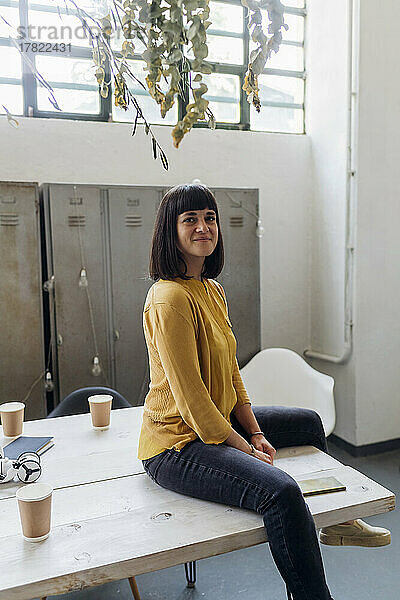 Lächelnde Geschäftsfrau sitzt am Schreibtisch am Arbeitsplatz
