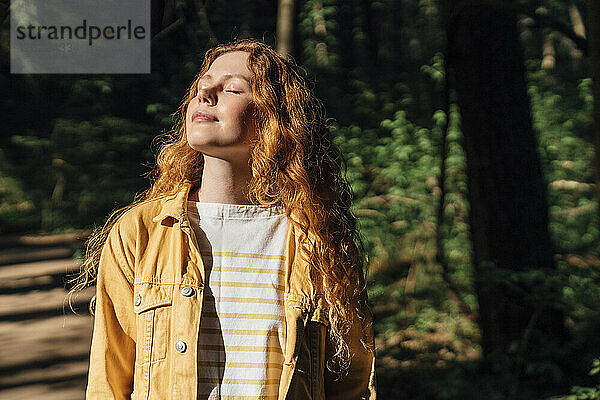 Frau mit geschlossenen Augen genießt das Sonnenlicht im Wald