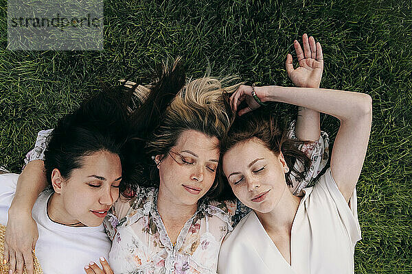 Friends with eyes closed lying on grass at park