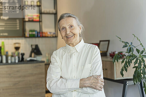 Glückliche ältere Frau mit verschränkten Armen steht im Café