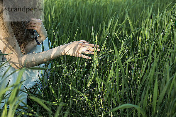Junge Frau berührt Gras im Feld
