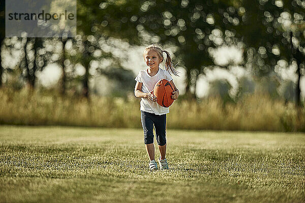 Smiling girl with rugby ball walking at sports field