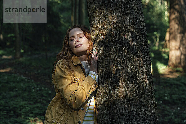 Junge Frau mit geschlossenen Augen umarmt Baum im Wald