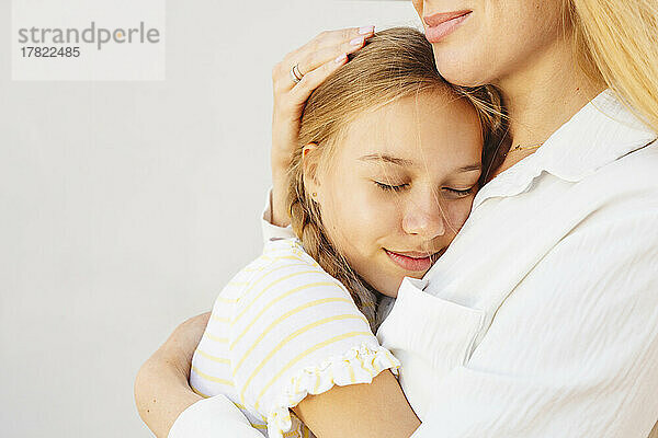 Lächelnde Frau umarmt Tochter vor der Wand