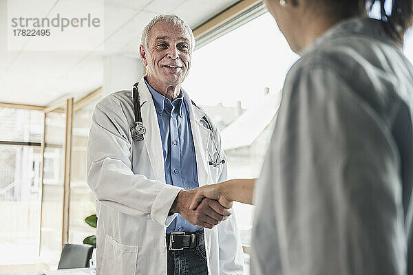 Happy doctor shaking hand with patient in medical clinic