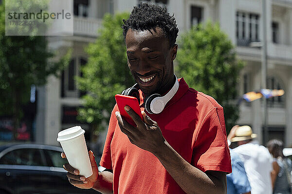 Lächelnder Mann mit Kaffeetasse und Mobiltelefon