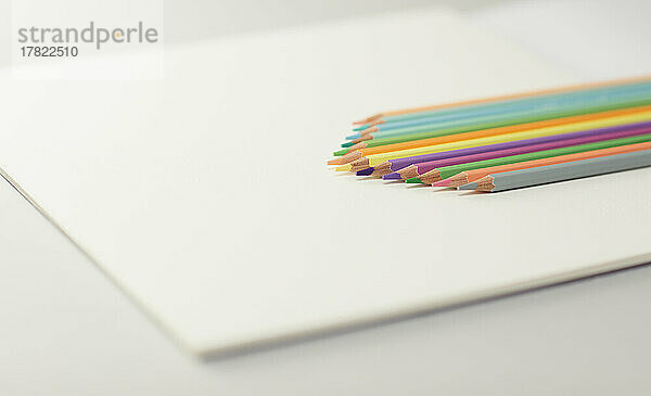Studioaufnahme einer Reihe von Buntstiften  die auf einem Zeichenpapierblock liegen