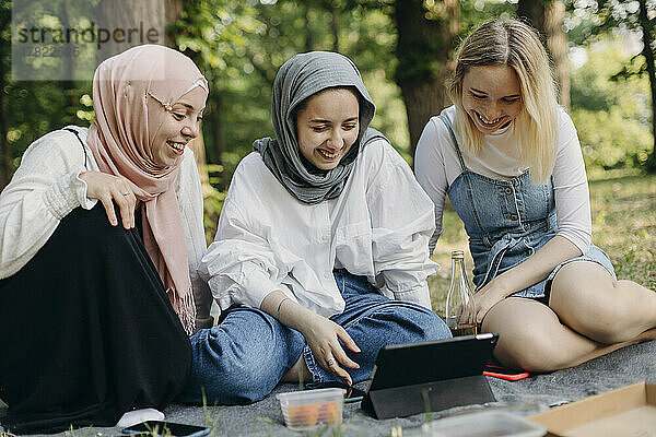 Fröhliche Freunde teilen sich im Park einen Tablet-PC