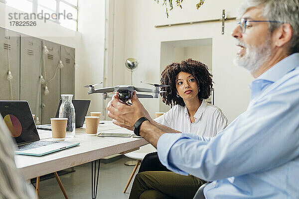 Geschäftsfrau blickt Geschäftsmann mit Drohne im Büro an