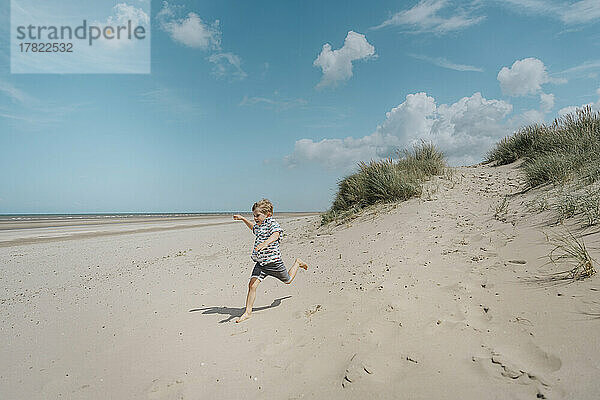 Fröhlicher Junge  der an einem sonnigen Tag am Strand läuft