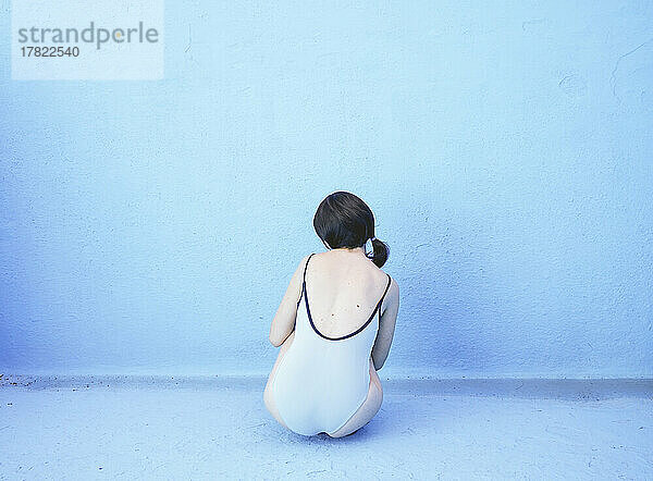Frau sitzt vor blauer Wand