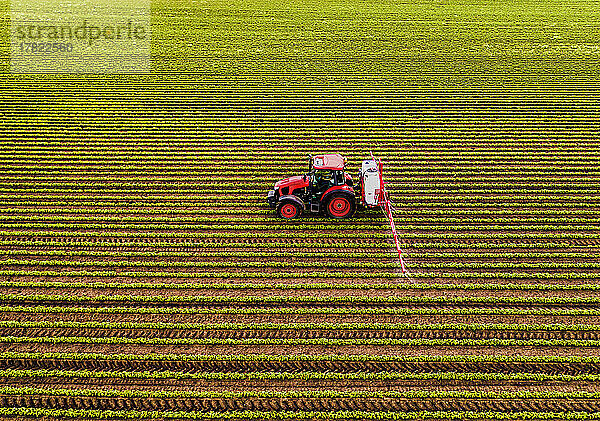Traktor mit Feldspritze auf Sojabohnenfeld bei Sonnenuntergang