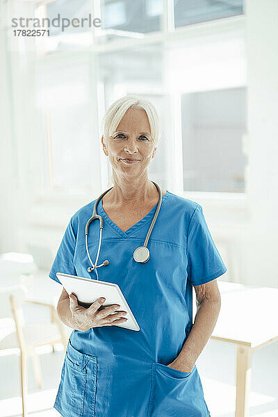 Lächelnde Ärztin hält Tablet-PC stehend mit der Hand in der Tasche