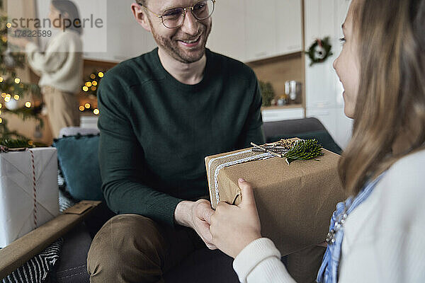 Lächelndes Mädchen  das dem Vater zu Hause ein Weihnachtsgeschenk gibt