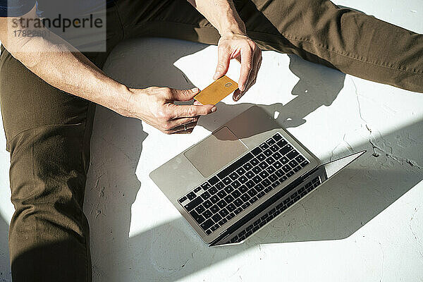 Geschäftsmann macht Online-Einkäufe und sitzt mit Kreditkarte und Laptop auf dem Boden