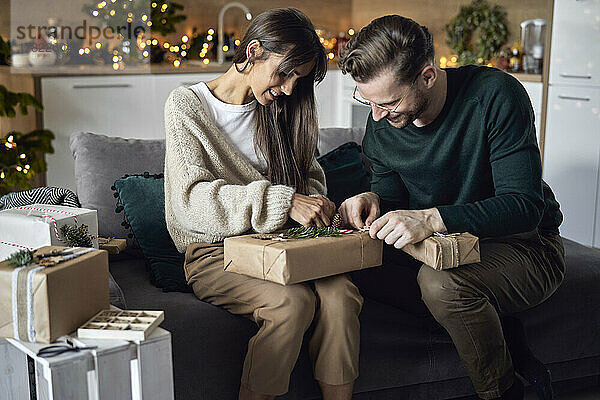 Lächelnde Frau und Mann  die zu Hause auf dem Sofa sitzen und Weihnachtsgeschenk einpacken