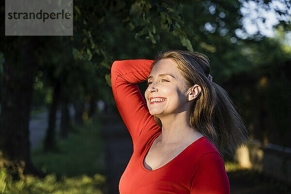 Glückliche Frau mit der Hand im Haar  die das Sonnenlicht genießt