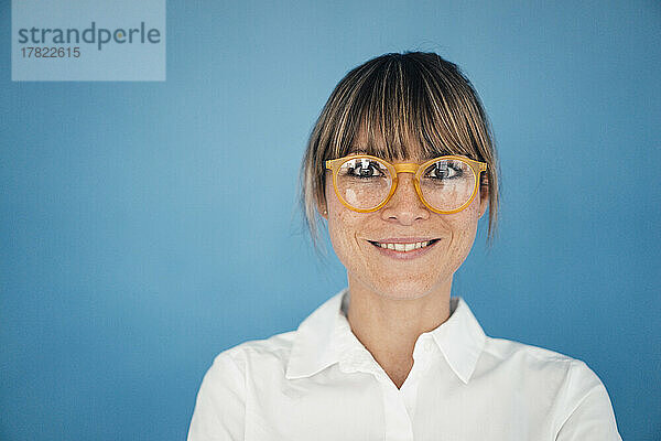 Lächelnde Geschäftsfrau mit Brille vor blauem Hintergrund