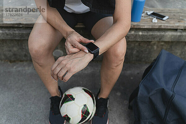 Frau mit Fußball überprüft die Zeit in einer Smartwatch