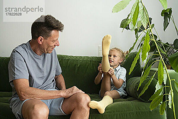 Mann schaut Tochter in Socken an  die auf Sofa sitzt