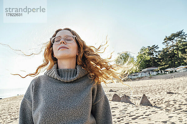 Junge Frau mit geschlossenen Augen genießt die frische Luft am Strand
