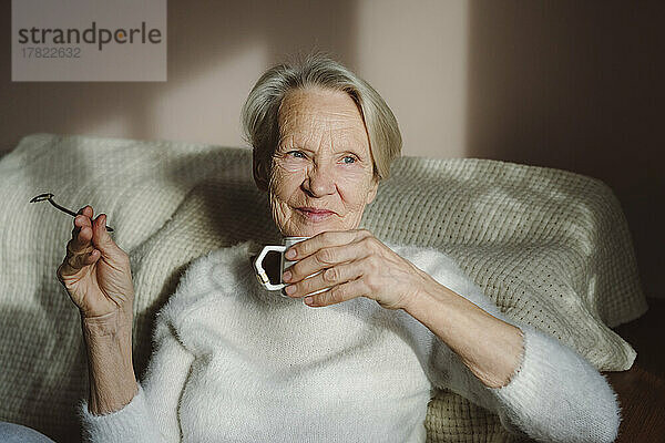 Glückliche ältere Frau mit Kaffeetasse  die zu Hause sitzt