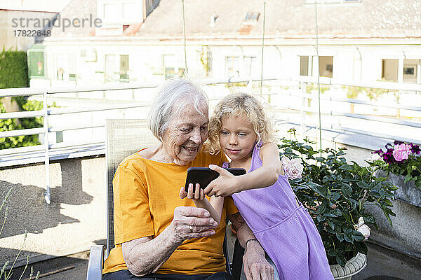 Enkelin zeigt Großmutter auf dem Balkon ihr Mobiltelefon