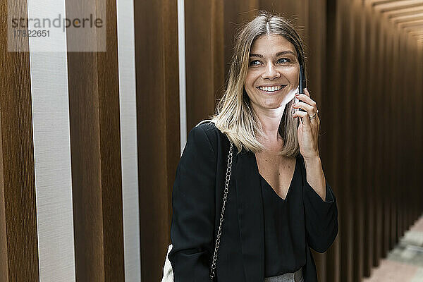 Lächelnde Geschäftsfrau  die auf dem Hotelflur mit dem Mobiltelefon telefoniert