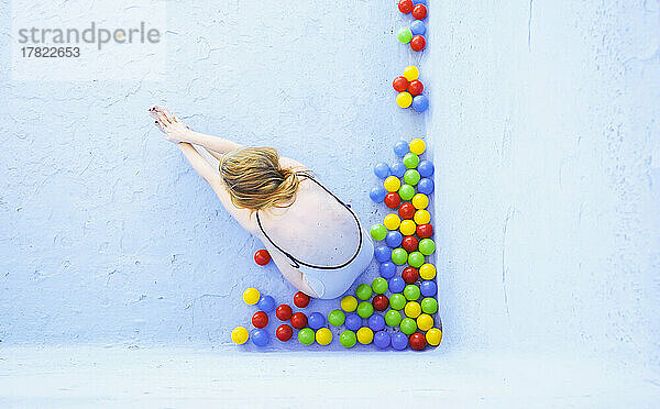 Woman doing yoga sitting by multi colored balls in empty swimming pool